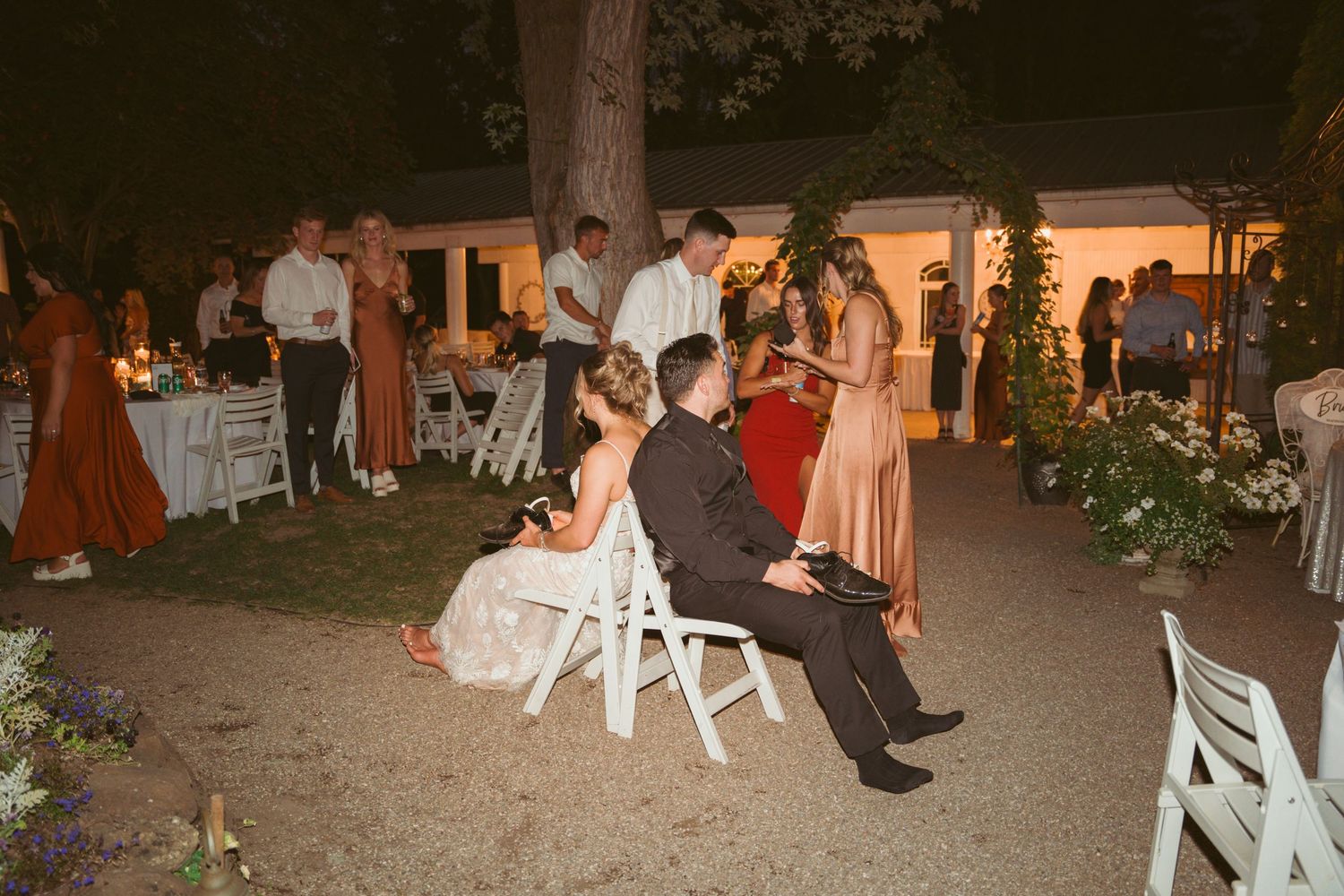 Wedding guests seated on white chairs at outdoor nighttime reception.