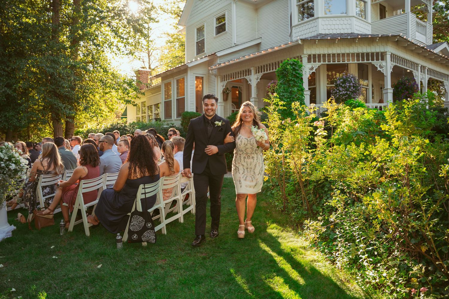 Wedding guests dance and celebrate on a lush green lawn at sunset during an outdoor garden reception.
