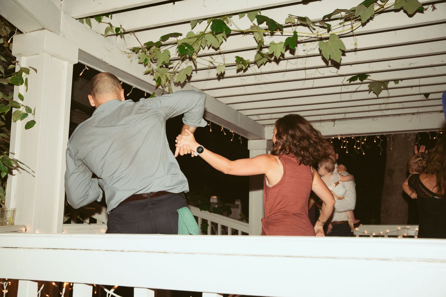 People dancing under a white pergola decorated with hanging vines.