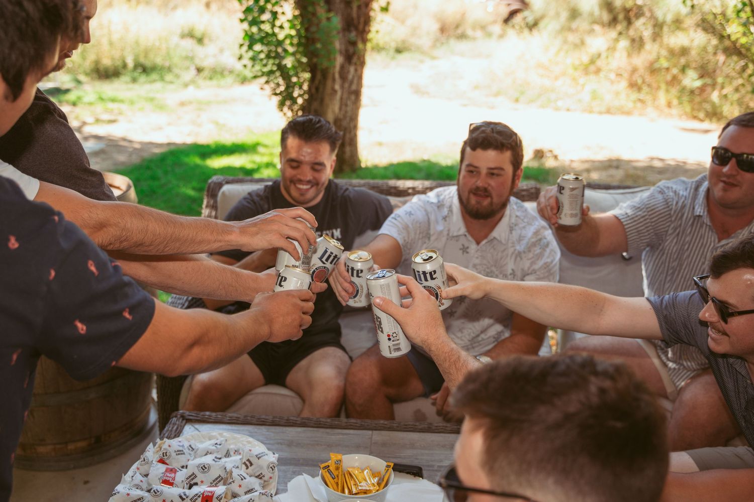 Friends playing cards together outdoors on a sunny day around a wooden table.