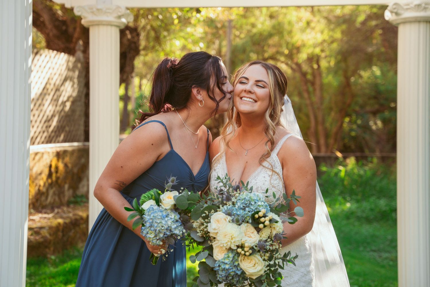 Intimate moment captured under white pergola with blue and white floral bouquets.