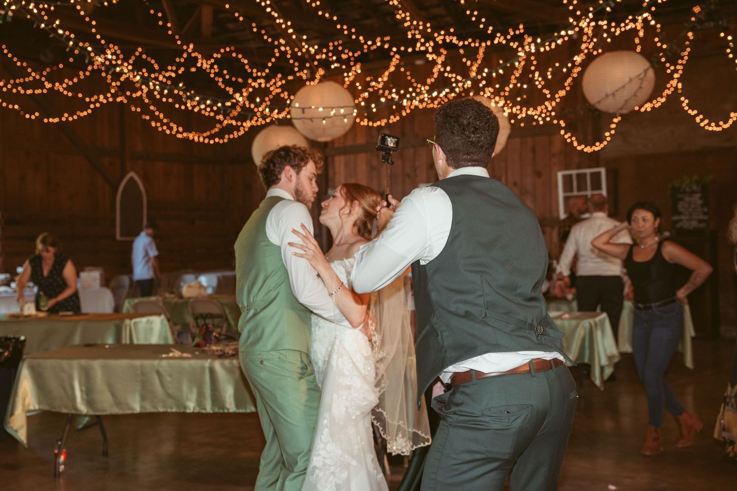Couples dancing together under glowing string lights at an elegant indoor wedding reception.
