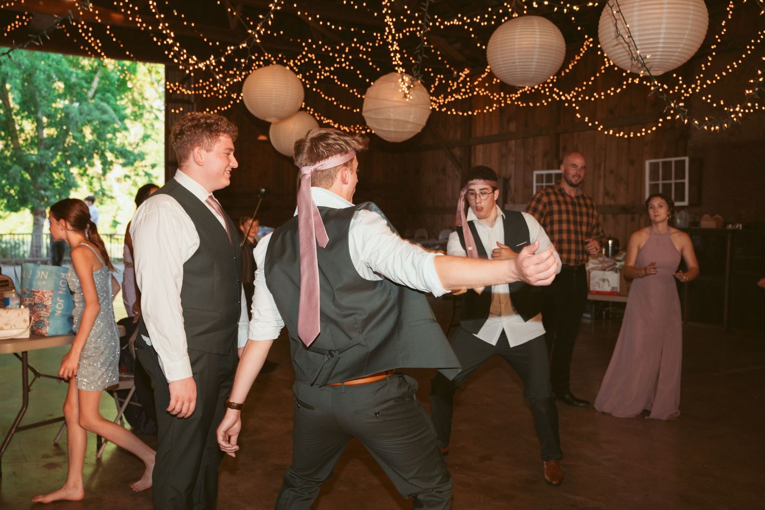 Wedding party dancing and having fun under decorative string lights and paper lanterns.