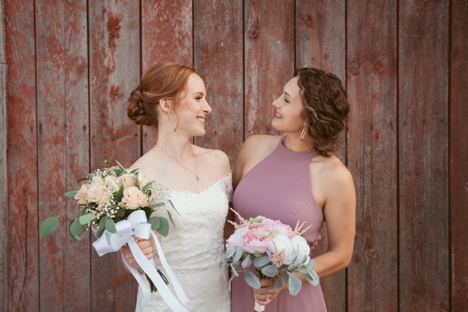 Candid wedding party moment captured against rustic red barn background.
