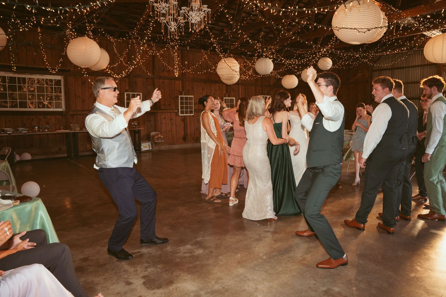 Wedding celebration with synchronized dancing under warm string lights in a rustic barn.