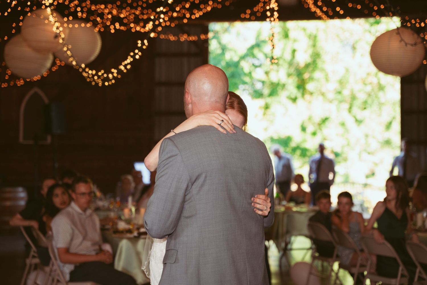 A romantic dance moment in a barn reception with warm fairy lights creating an intimate atmosphere.