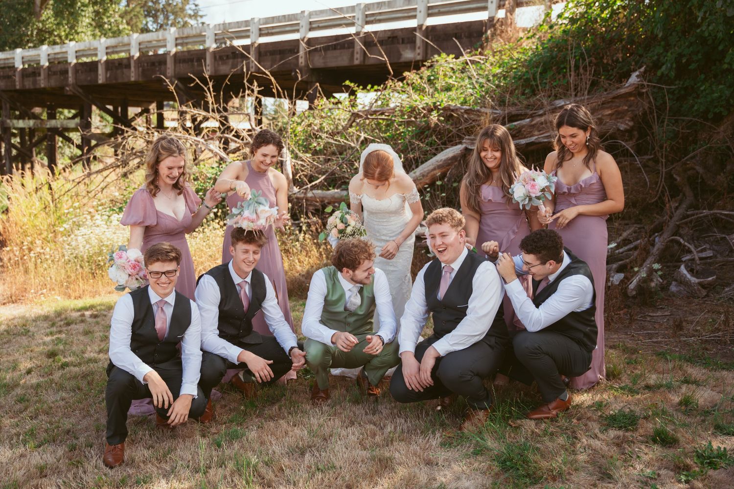 Wedding party members relaxing casually on a grassy slope in coordinated attire.