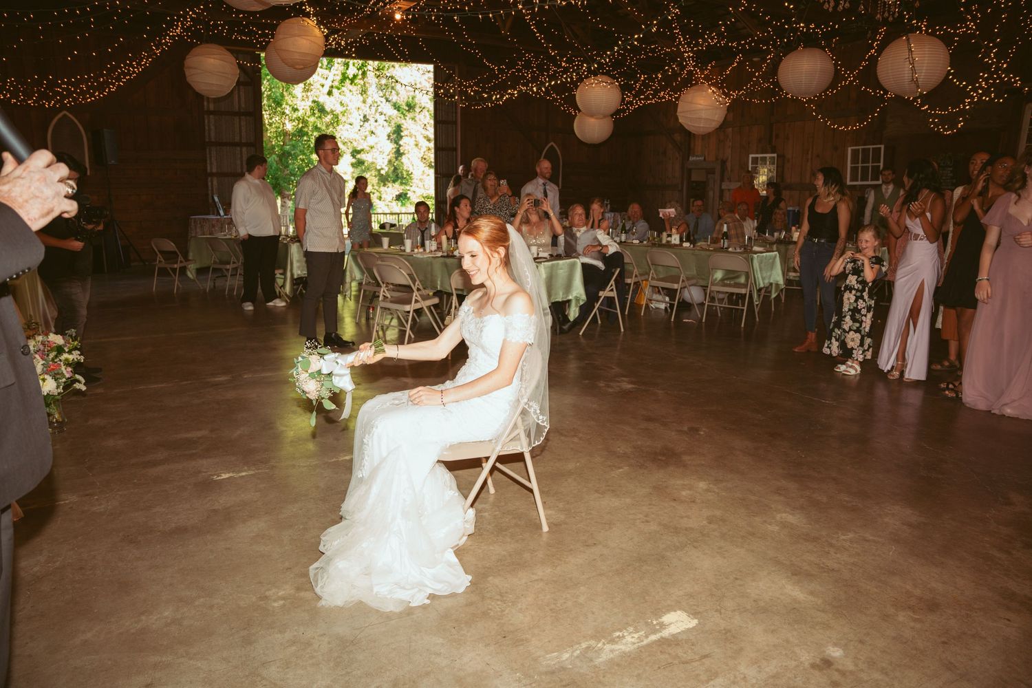 Wedding reception setup in a rustic barn with string lights and paper lanterns.