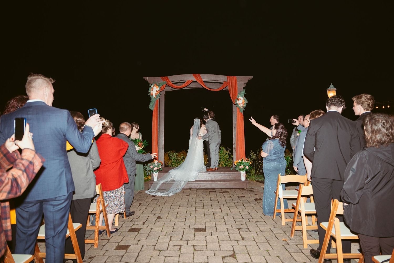 Outdoor wedding venue at night with string lights illuminating rows of wooden benches.