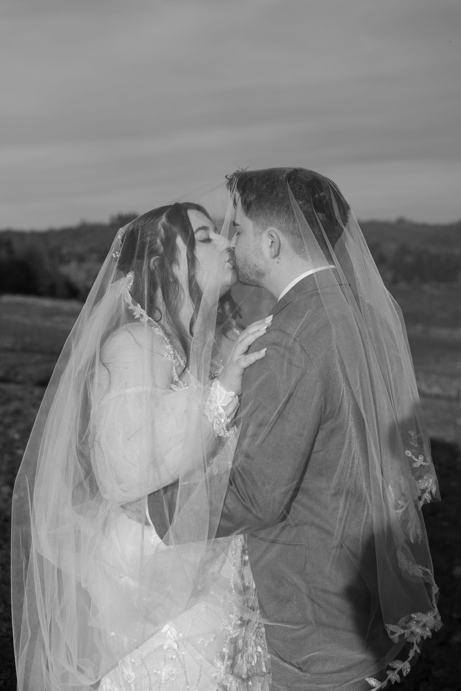 A romantic wedding couple shares an intimate moment under a veil in black and white.