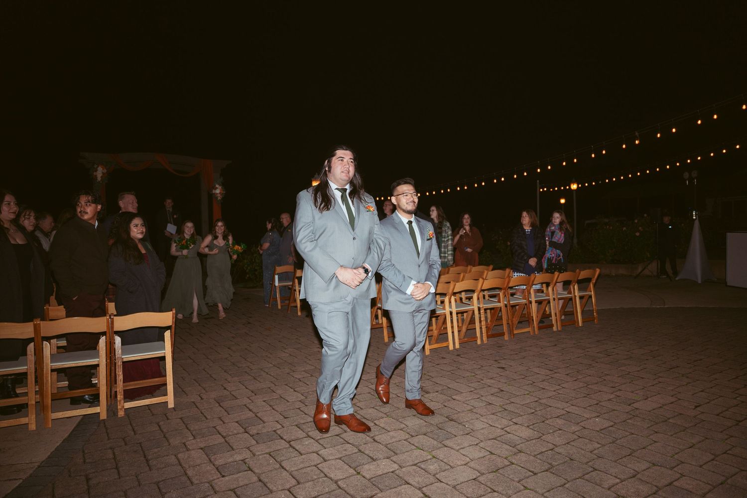 Outdoor wedding reception setup with glowing string lights and rustic wooden chairs.
