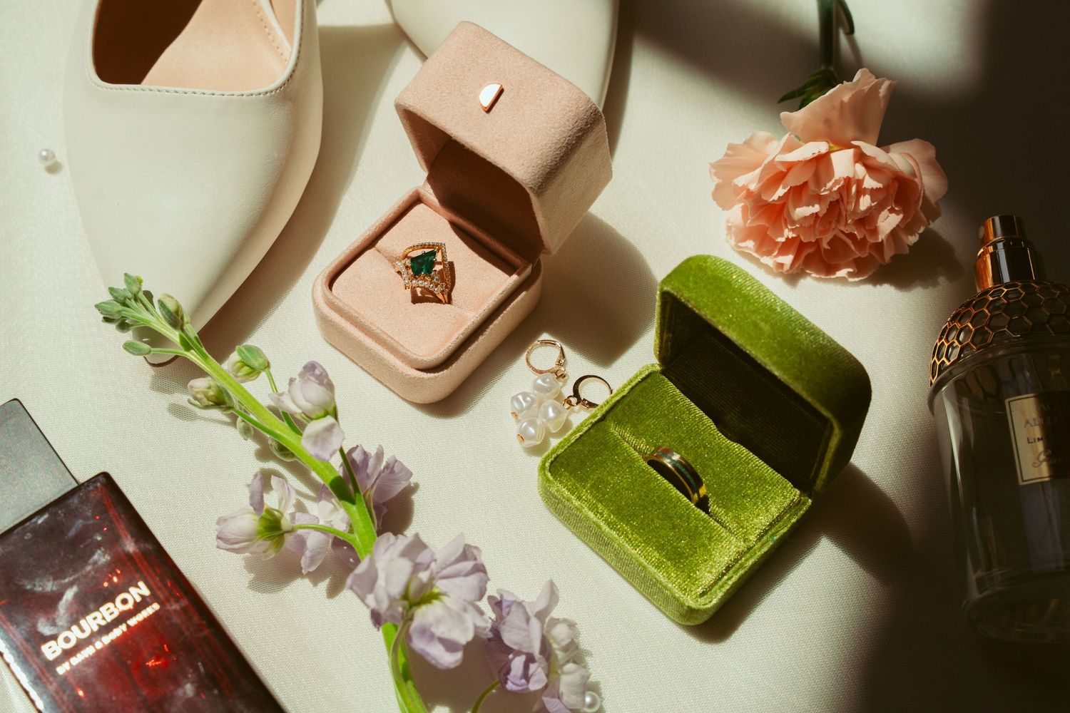 Wedding details including ring boxes, perfume bottles and floral elements in dramatic lighting.