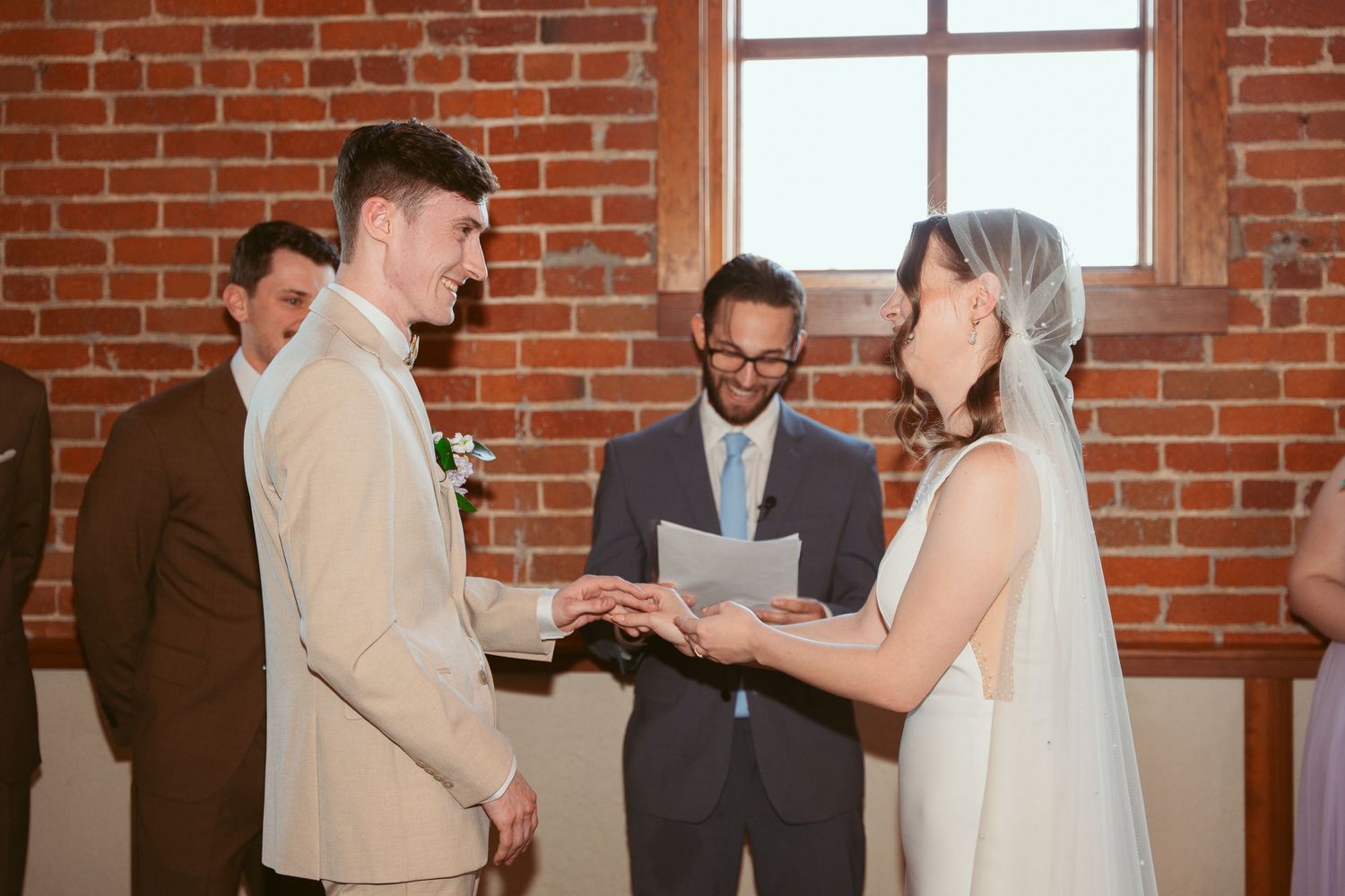 Couple sharing intimate moment during wedding ceremony in front of exposed brick wall backdrop.