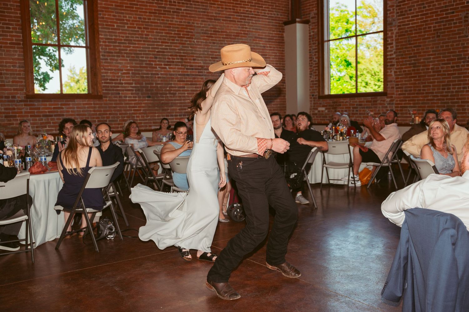 Wedding dance performance features a dramatic dip move in a rustic reception space.