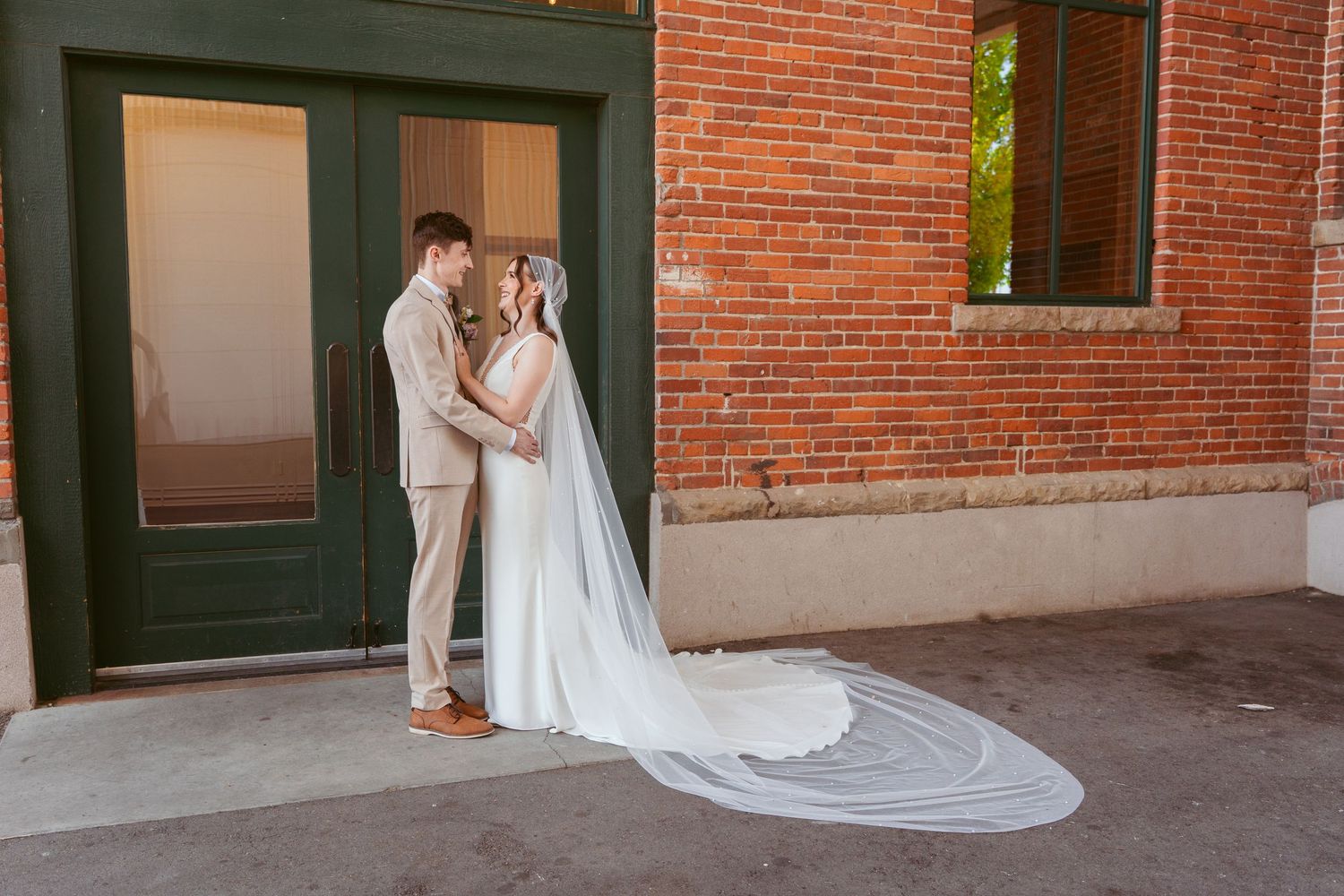 Wedding party poses along brick wall exterior in elegant formal attire.
