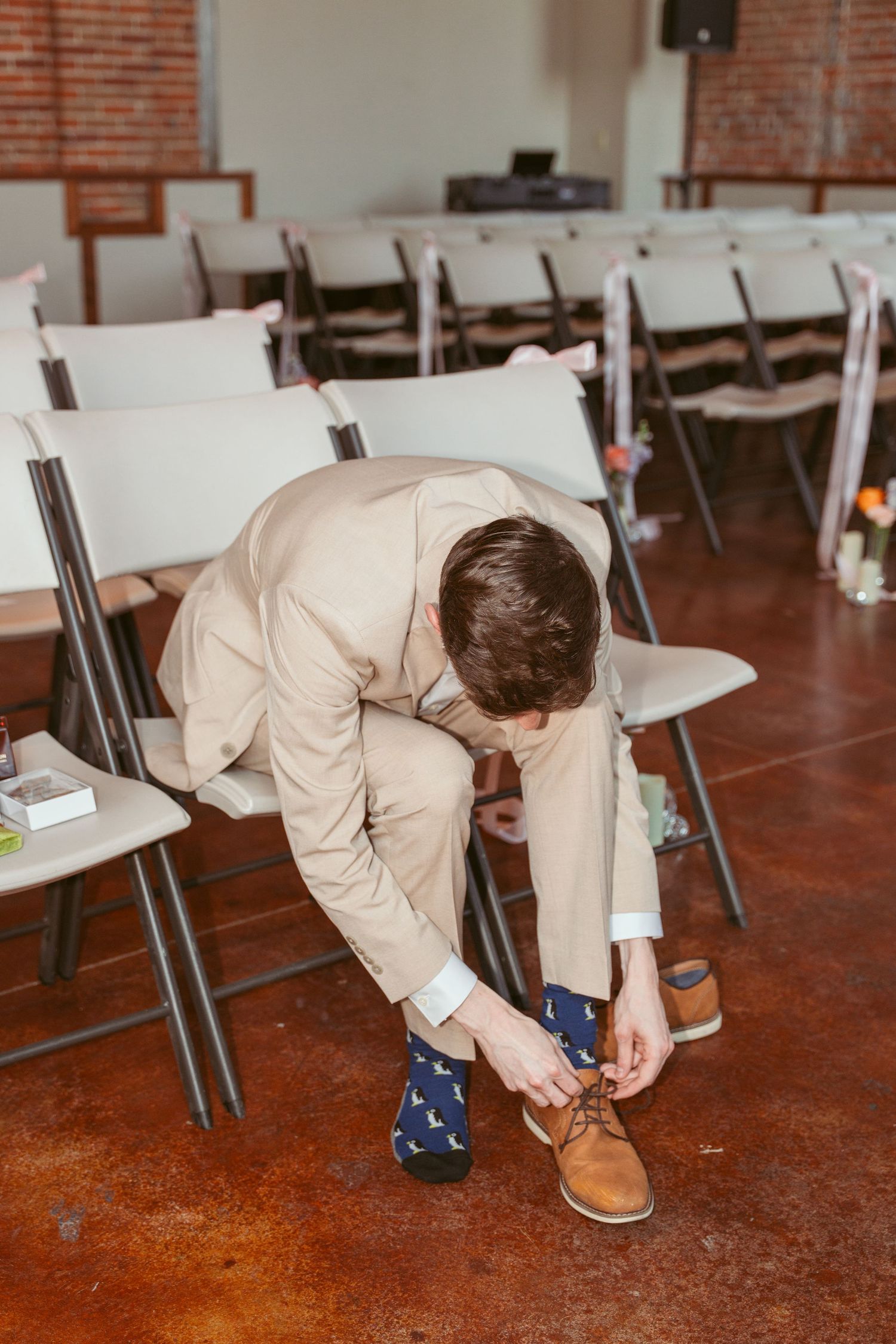 Someone in a beige suit bends down to adjust their brown leather shoes.