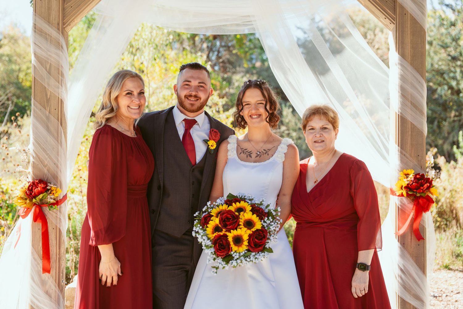 Wedding group in red and black attire gathered under decorated outdoor pavilion with sunflower bouquets.