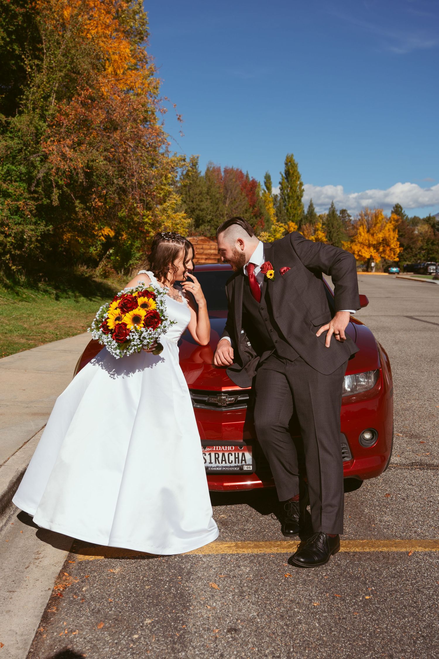 A joyful wedding moment against fall foliage and a red car.