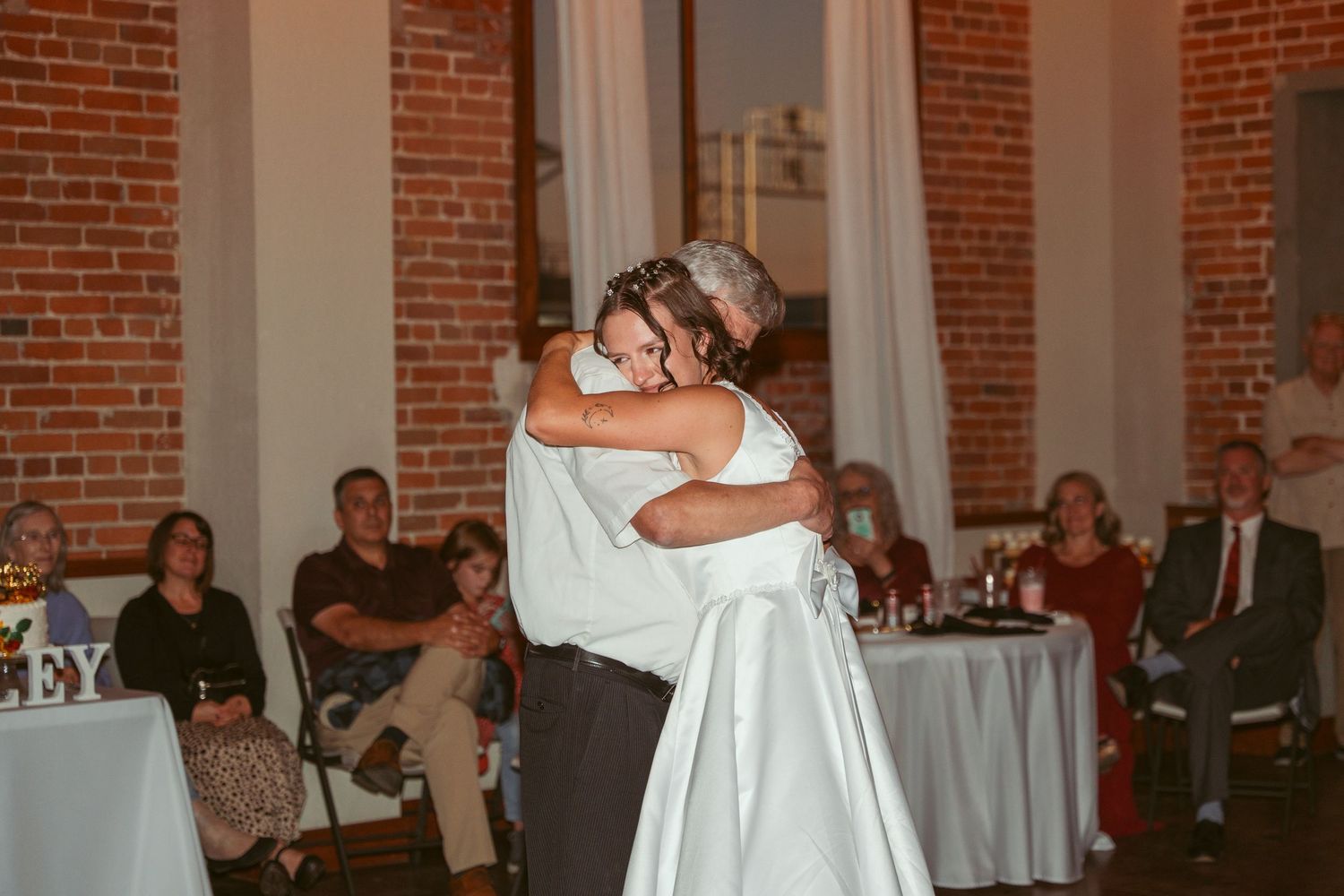 Couples dancing at an indoor wedding reception with exposed brick walls and string lights.