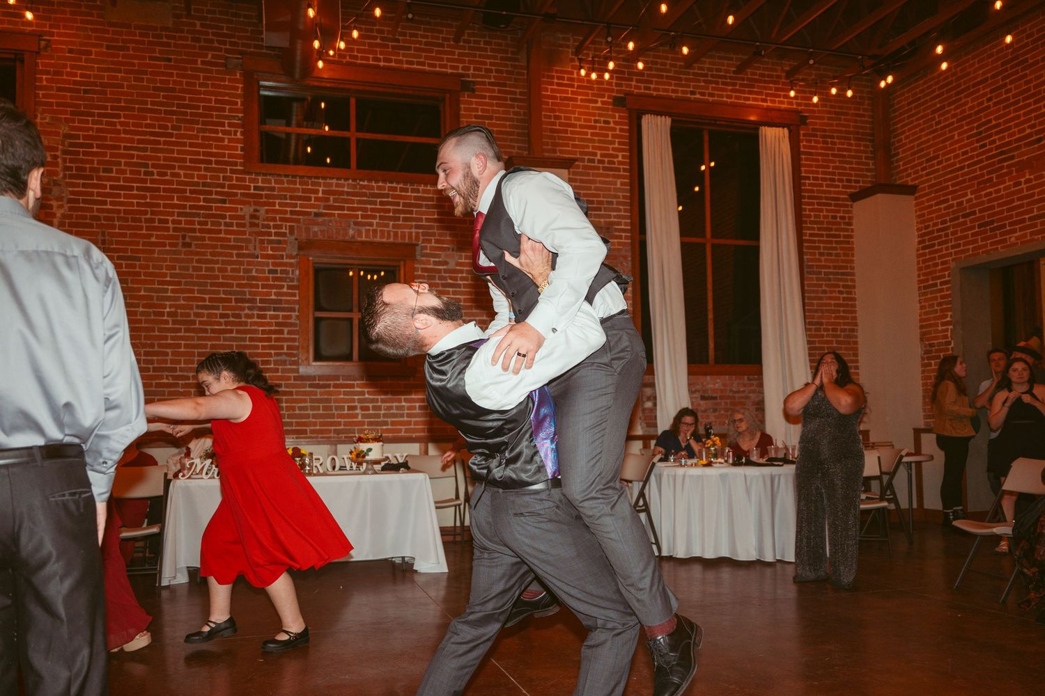 Dancers performing dramatic lifts and spins at a wedding reception in a brick venue.