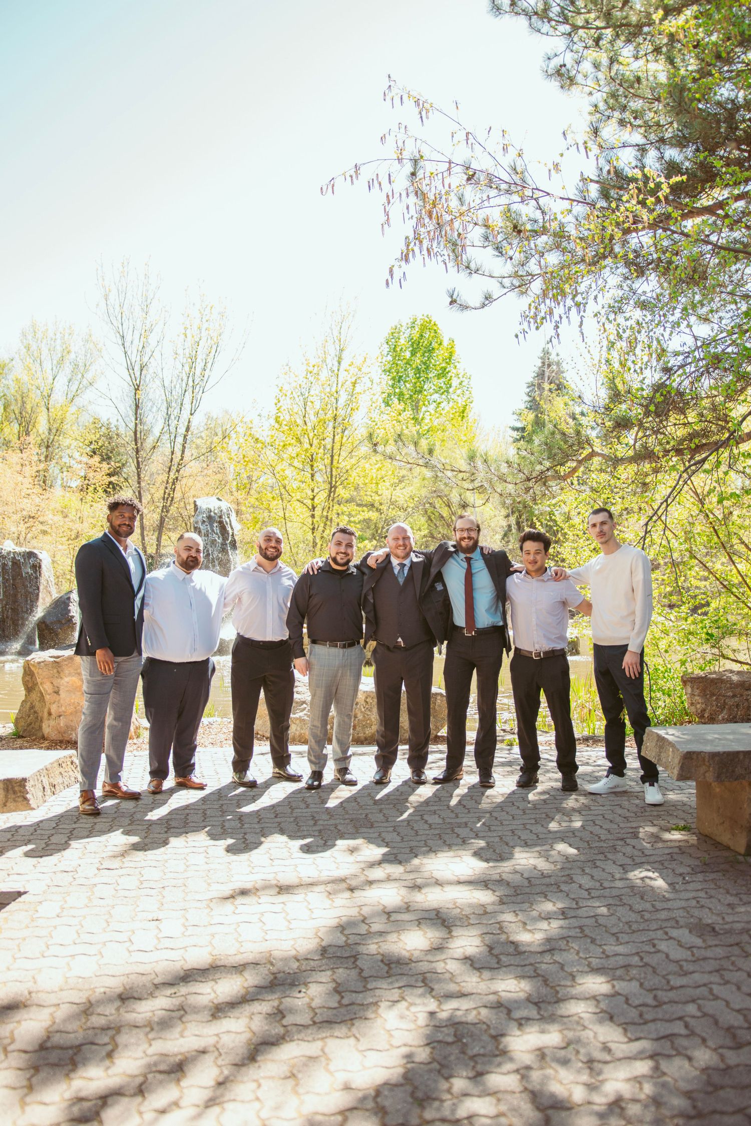 Wedding party members line up on a stone patio for formal photos.