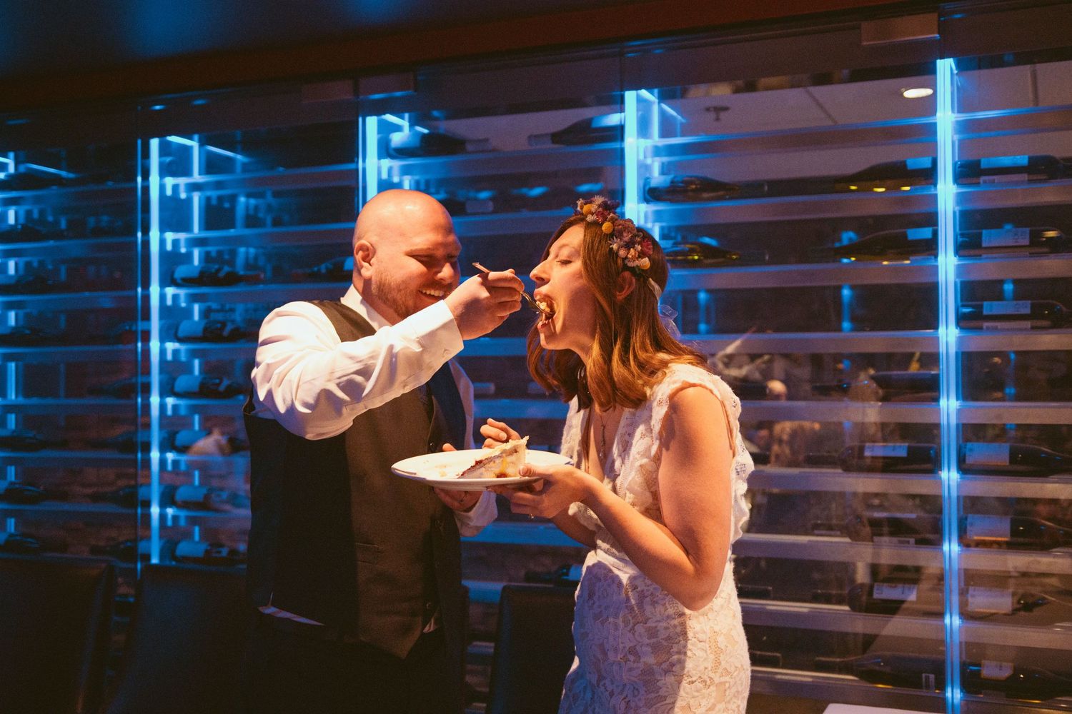 People dancing and celebrating at a reception with blue ambient lighting and white decor.