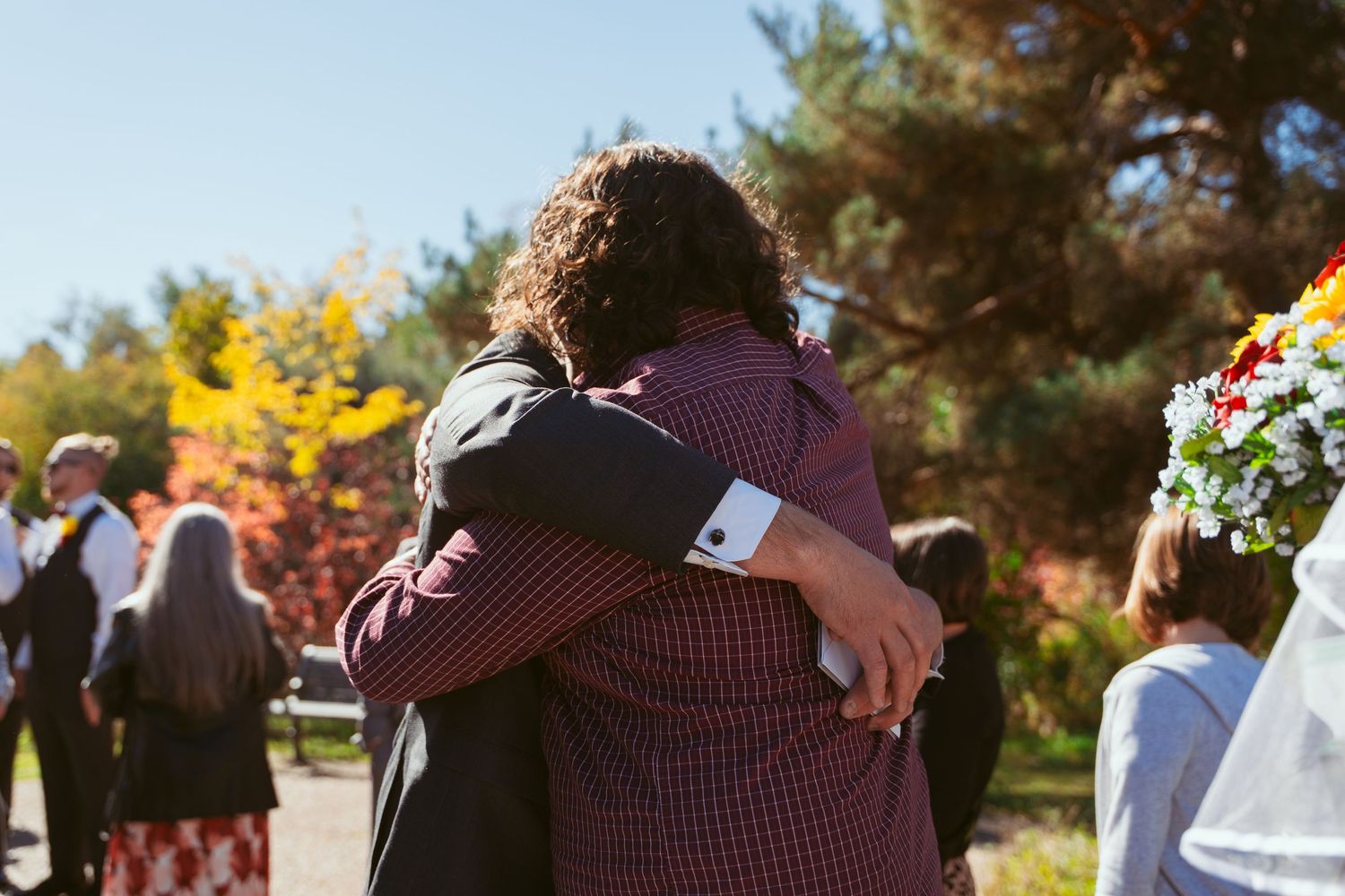 Wedding celebration with guests hugging and embracing outdoors during fall season.