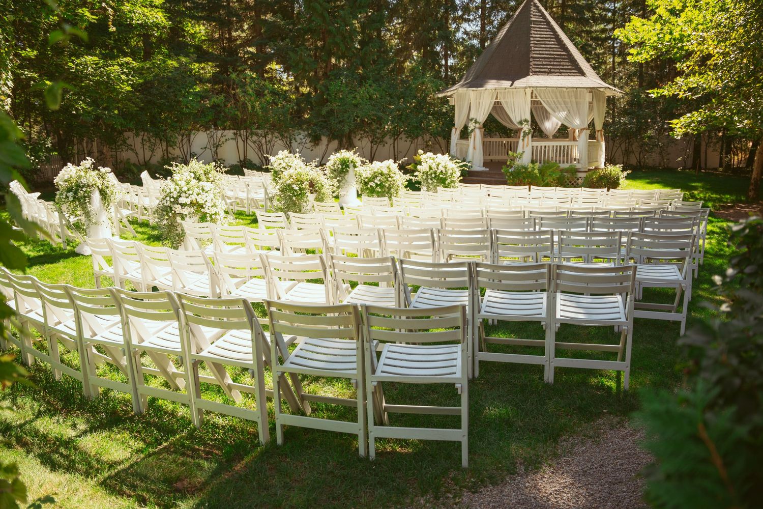 White folding chairs arranged in rows for an outdoor wedding ceremony under trees.