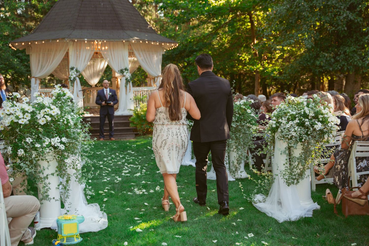 Elegant garden wedding ceremony with white decorations and natural greenery backdrop.