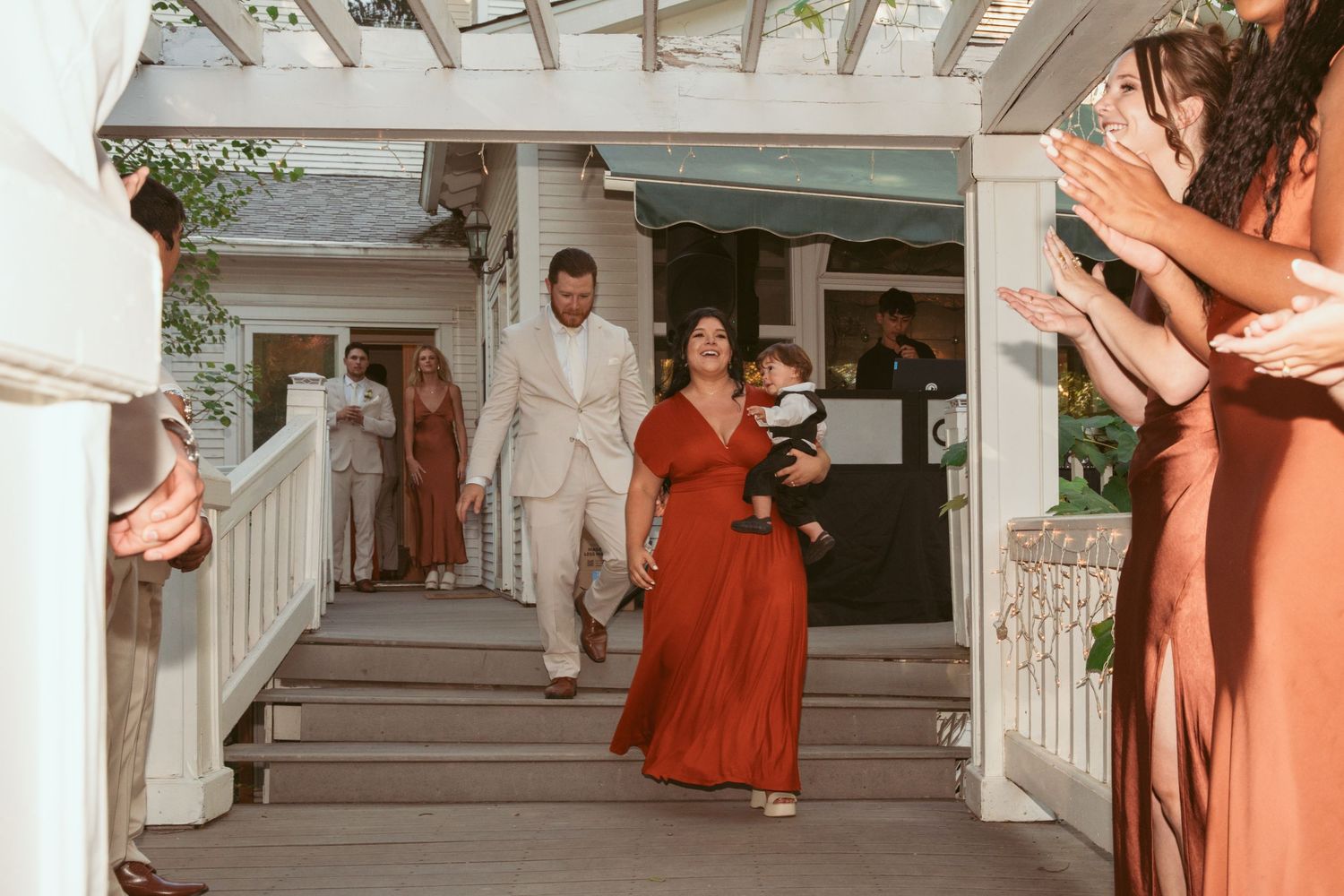 Wedding party members descend white porch stairs during a formal entrance.