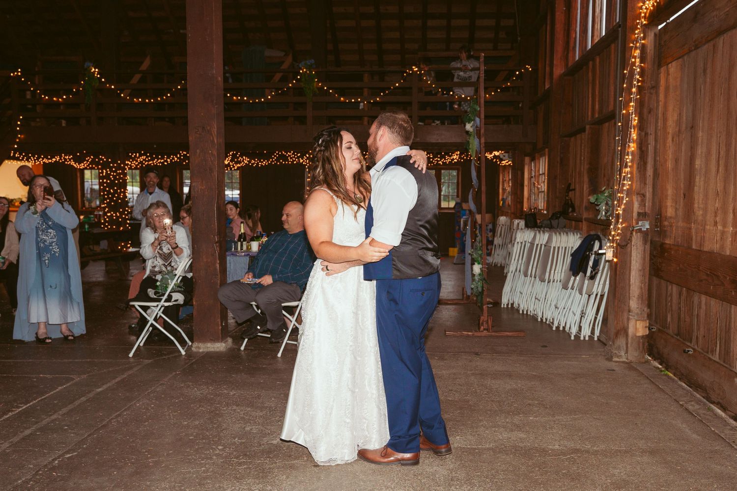 A couple dancing together in a rustic wooden barn decorated with string lights.