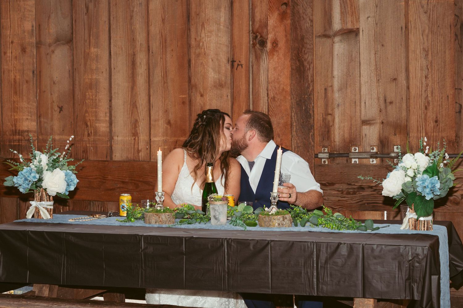 Head table decorated with floral arrangements in rustic barn wedding venue.