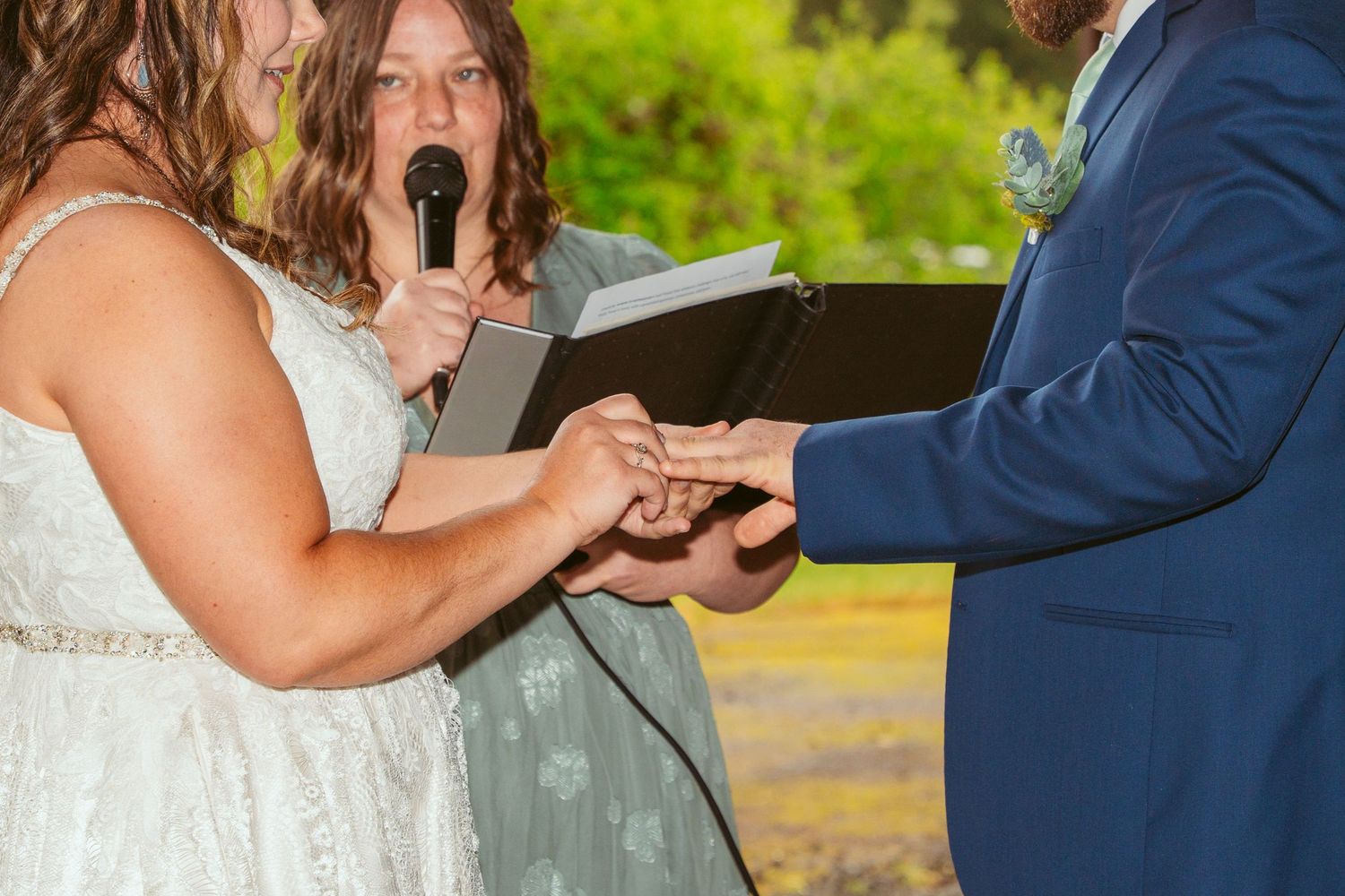 Wedding couple exchanges rings during ceremony in rustic barn setting.