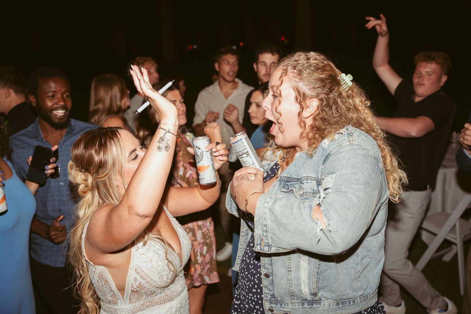 Energetic party guests dancing and singing together under string lights at an evening celebration.