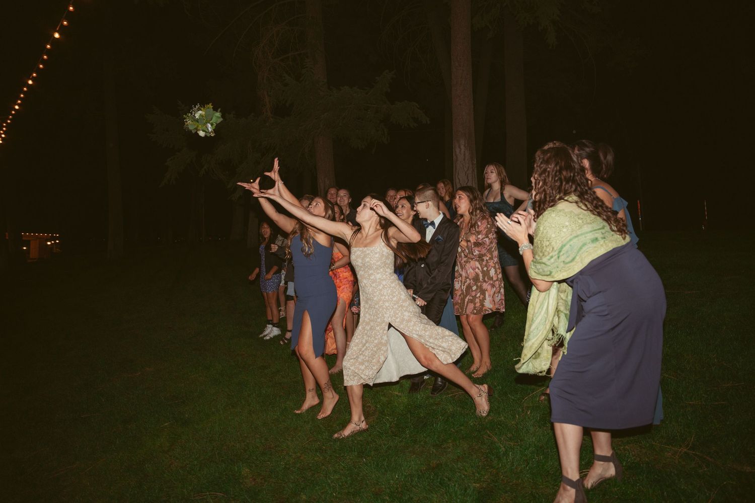 Wedding guests dance and celebrate on an outdoor dance floor at night under string lights.