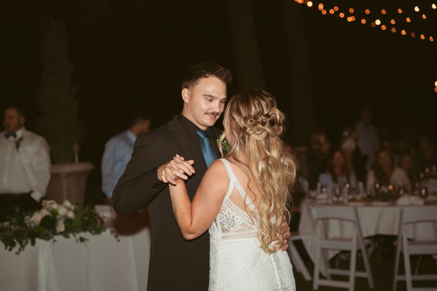 Wedding reception dance floor with string lights overhead and guests dancing.