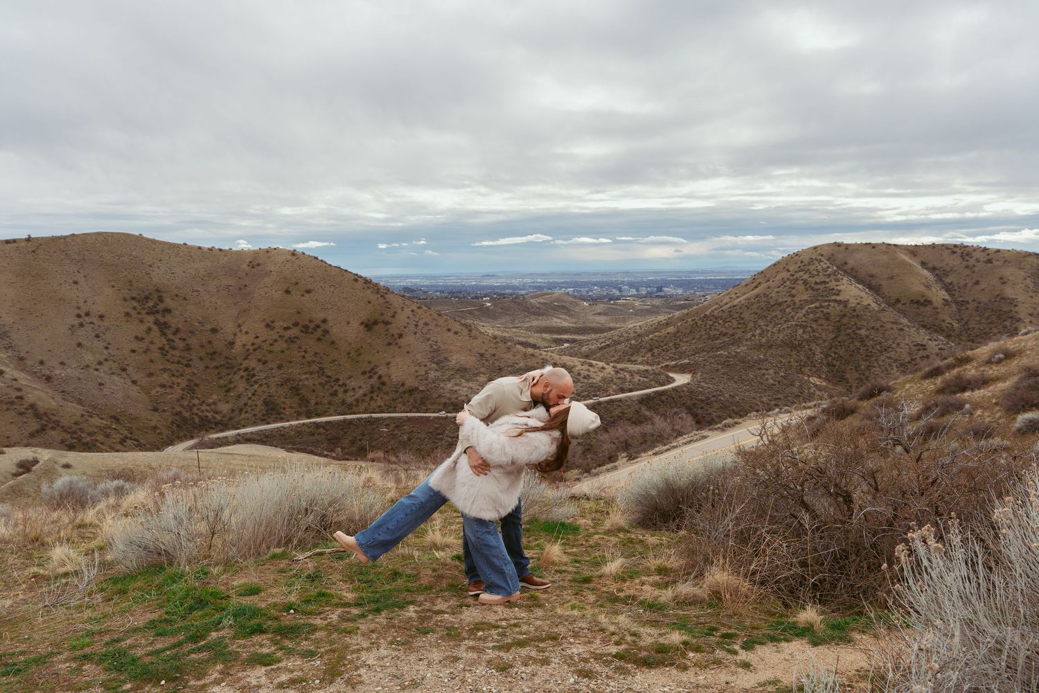 A panoramic view of rolling hills and mountains under cloudy skies in a desert landscape.