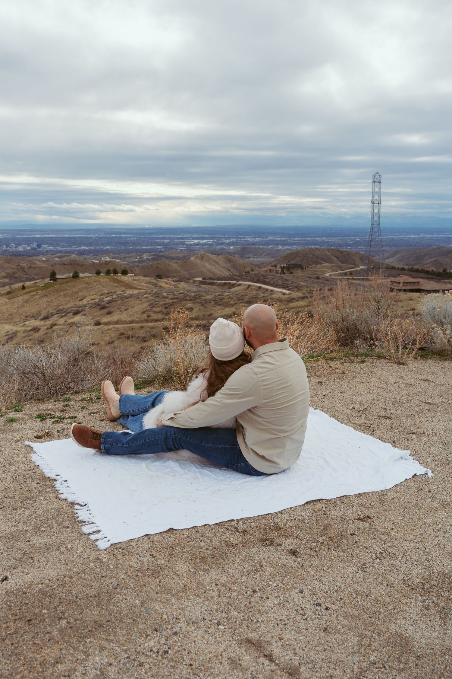 Someone relaxing on a white blanket overlooking a scenic desert valley with power lines in the distance.