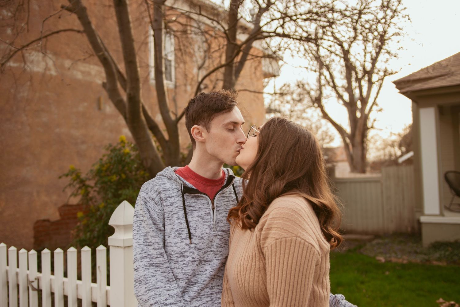 A sweet moment between a couple standing by a picket fence in autumn weather.