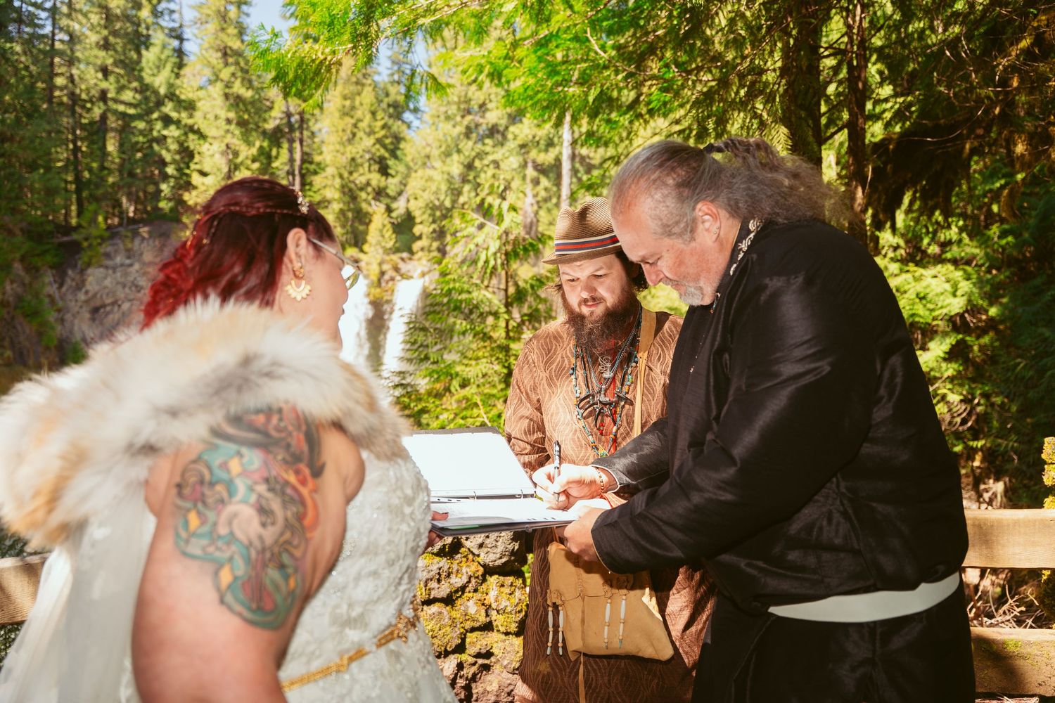 A couple shares a romantic moment during a sunset ceremony in a wooded outdoor setting.