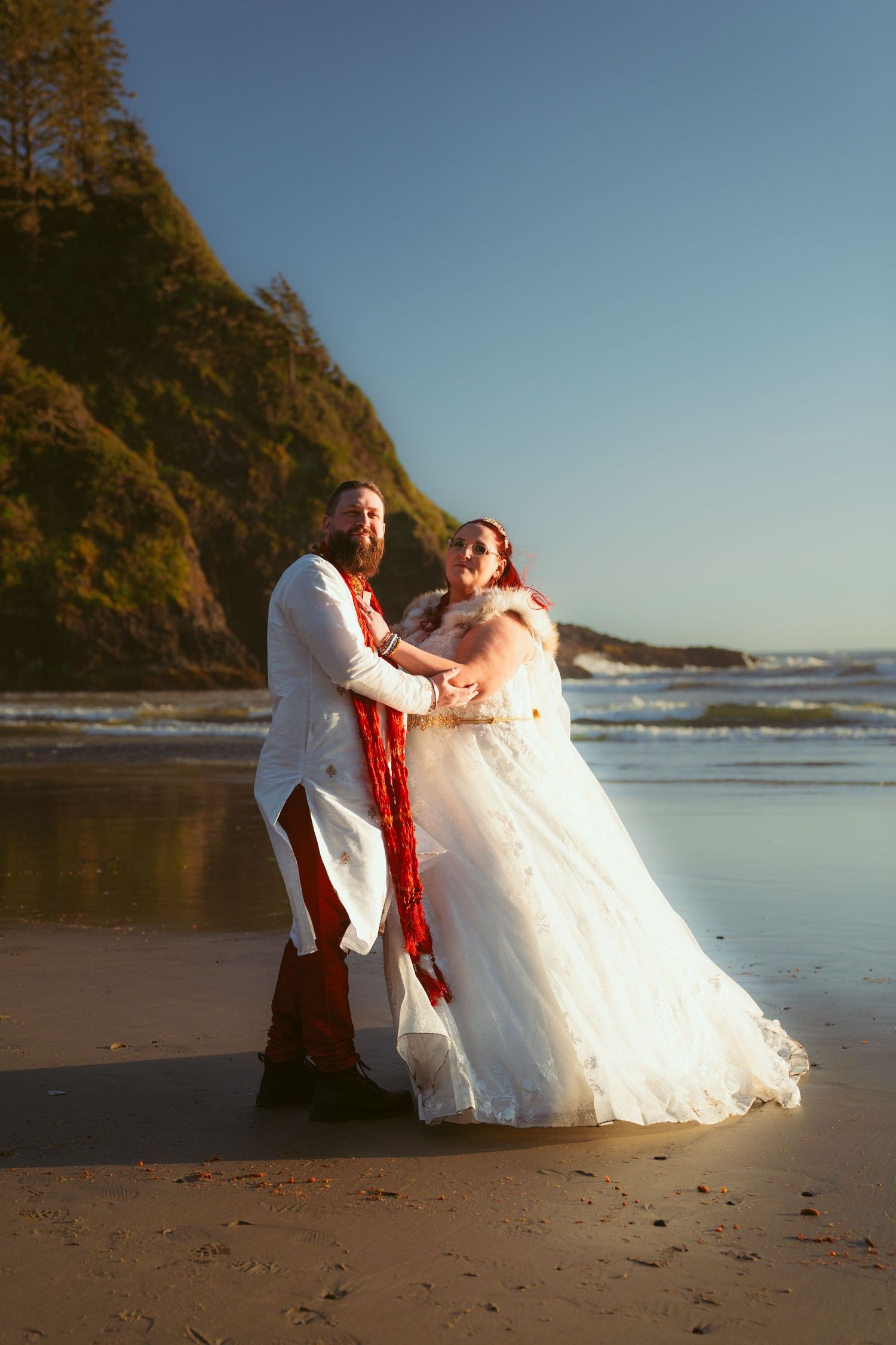 A couple shares a playful moment on a beach with dramatic coastal cliffs.