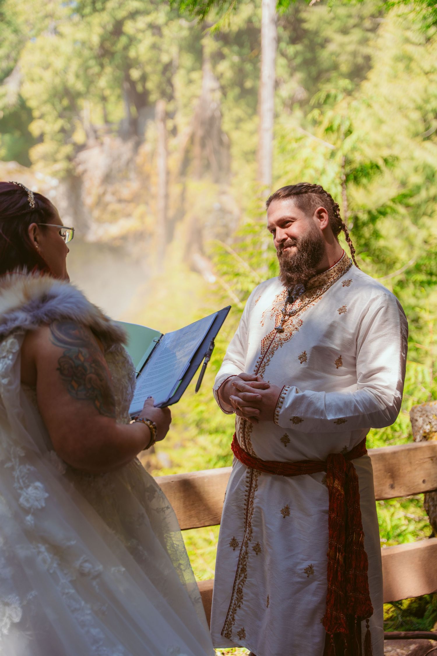 A couple exchanges vows during a forest wedding ceremony with sunlight filtering through the trees.