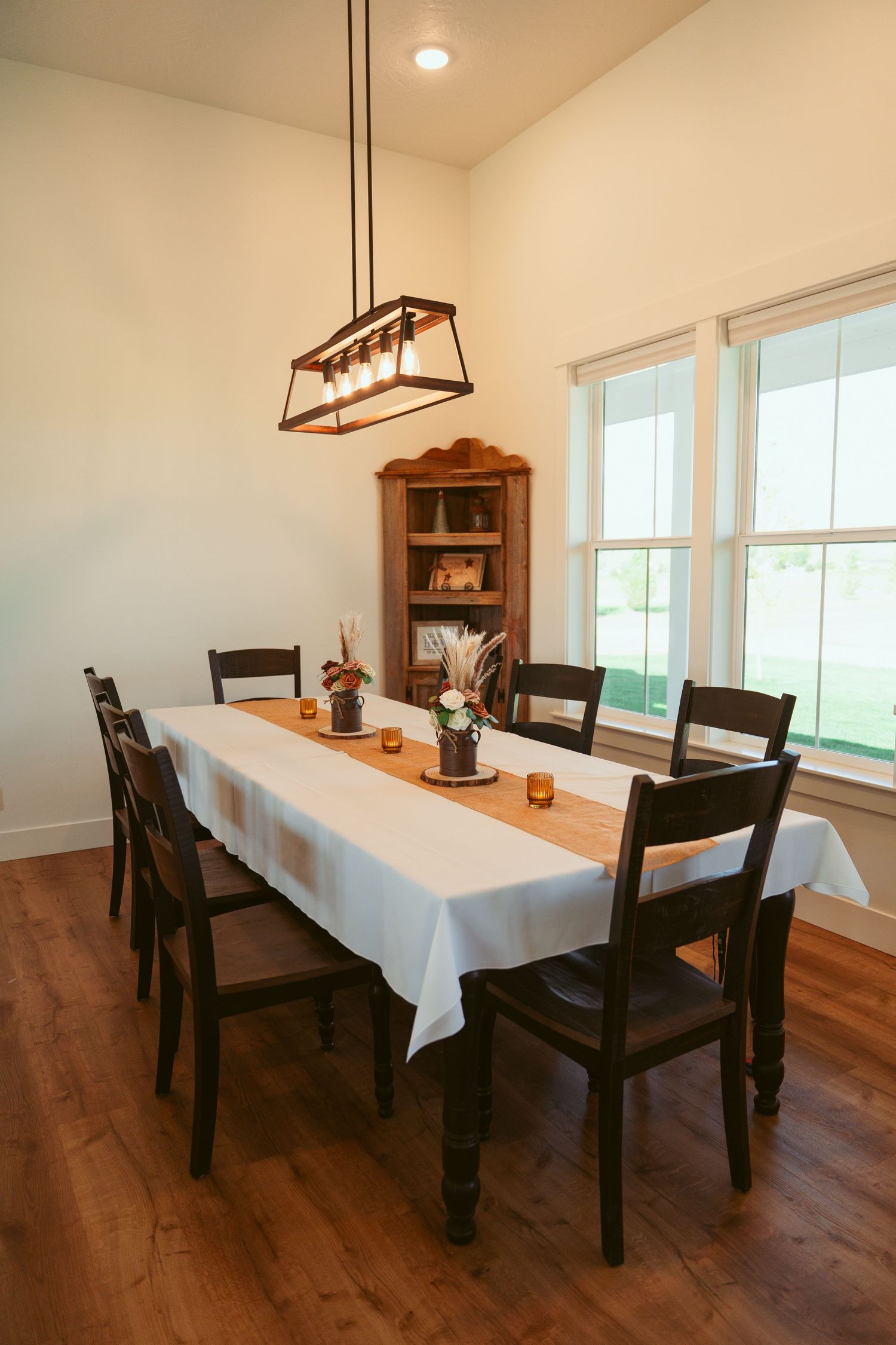 Dining room with white tablecloth, black chairs, and modern rectangular chandelier.
