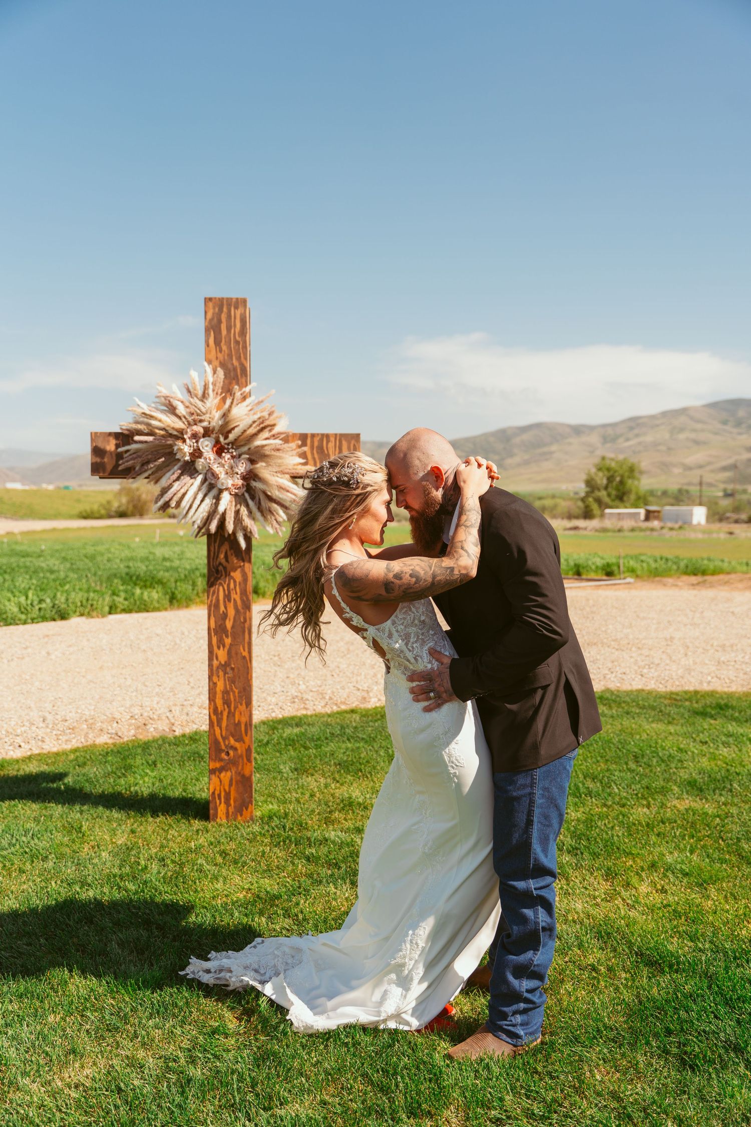 A couple in wedding attire dances playfully in a grassy field with mountains in the background.