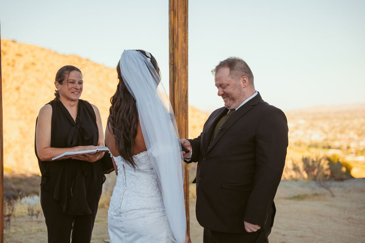 Wedding ceremony in progress under a wooden arch with desert mountains creating a scenic backdrop.