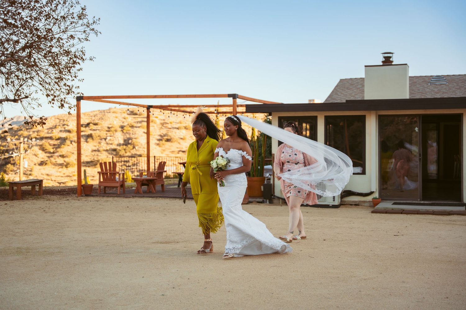 A bride in flowing white dress runs across a desert landscape at sunset.
