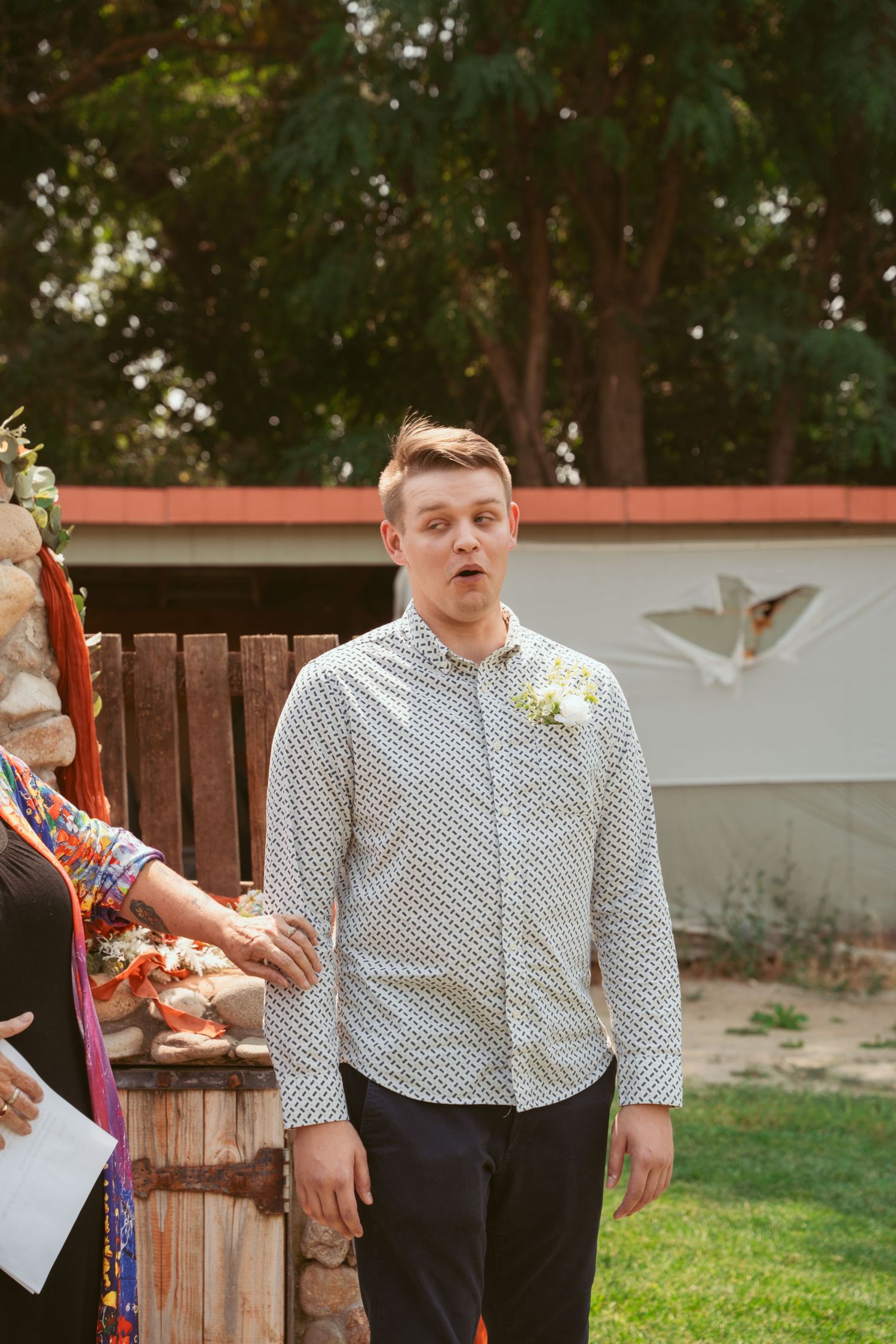 Wedding party members in formal attire standing outdoors near wooden fencing.