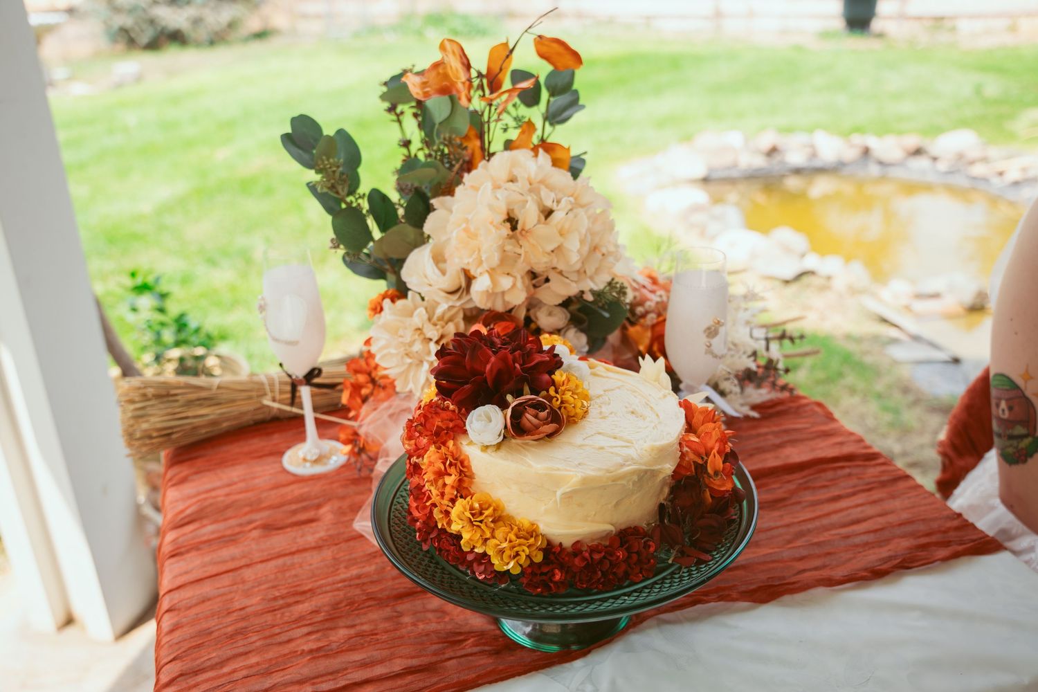 Wedding cake display with autumn decorations and orange table linens in outdoor garden setting.