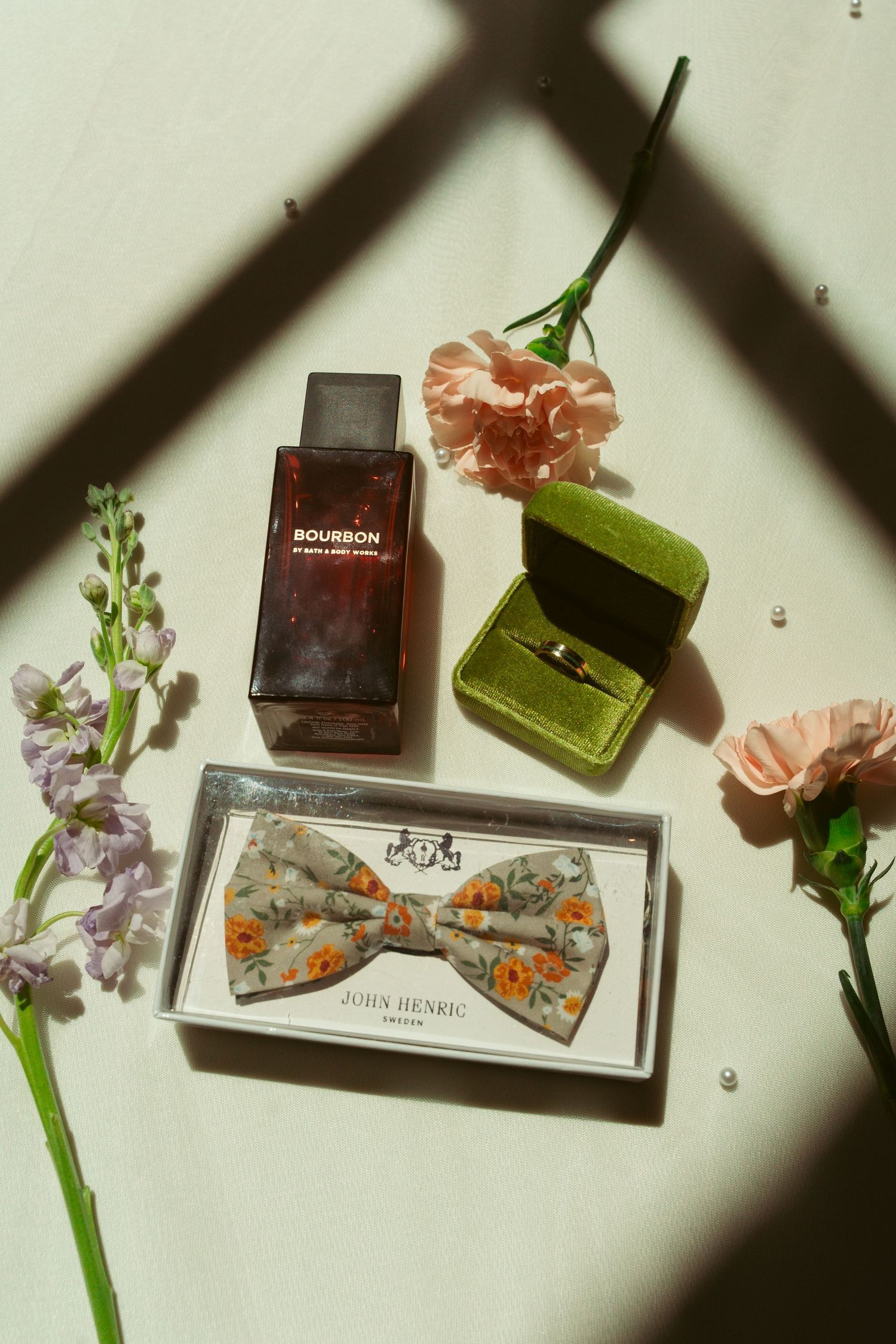 Wedding accessories including a floral bowtie, perfume bottles, and delicate flowers arranged on a light surface.