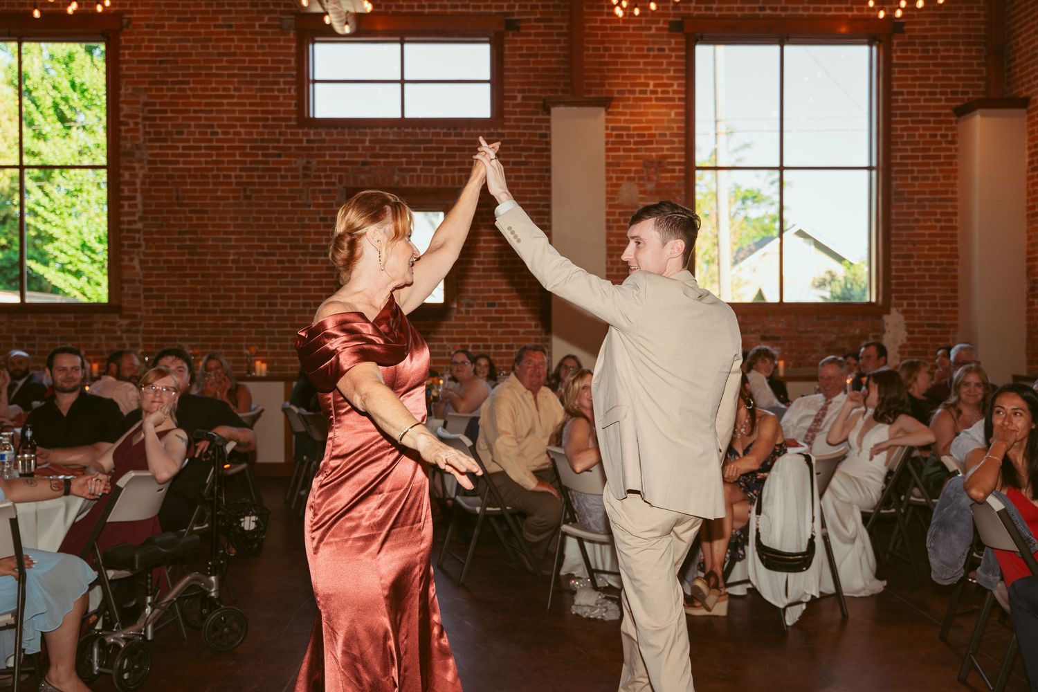 Wedding party members dance in formation during a reception in an industrial-style brick venue.